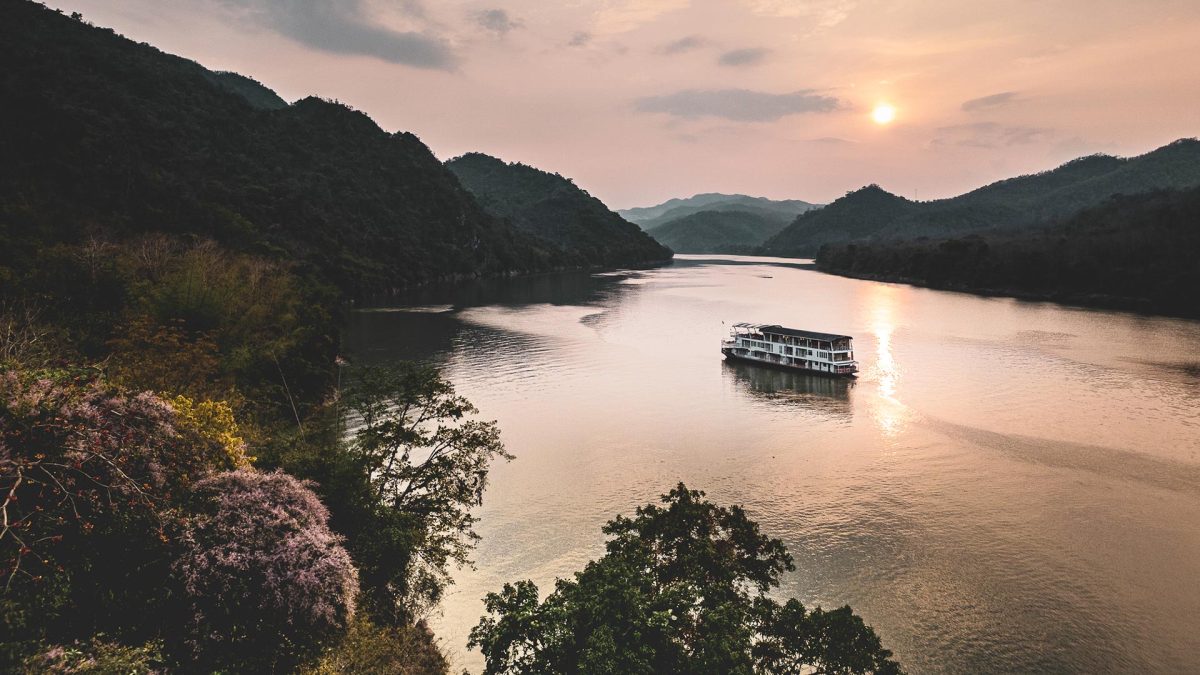 Mekong Kingdoms Bohème cruising a forested stretch of the Mekong near Luang Prabang at sunset