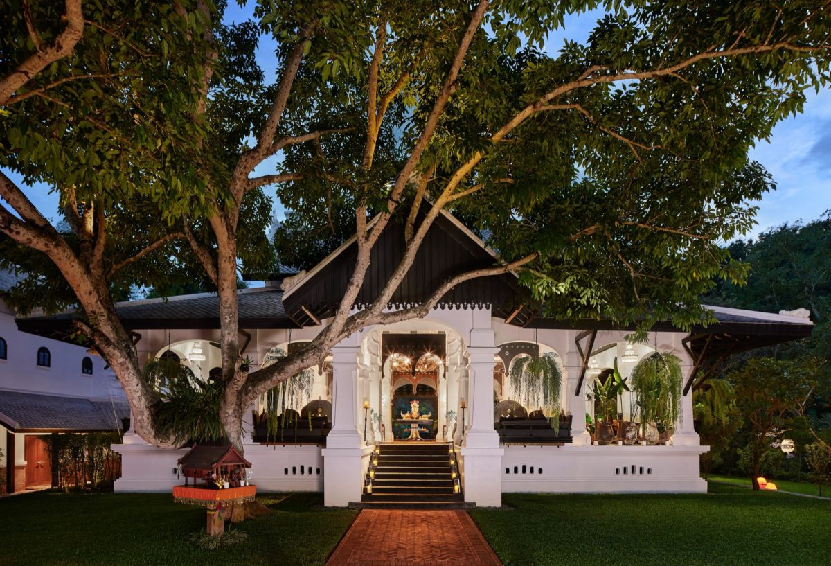 The Great House at Rosewood Luang Prabang at dusk, its lit terrace beneath a large tree