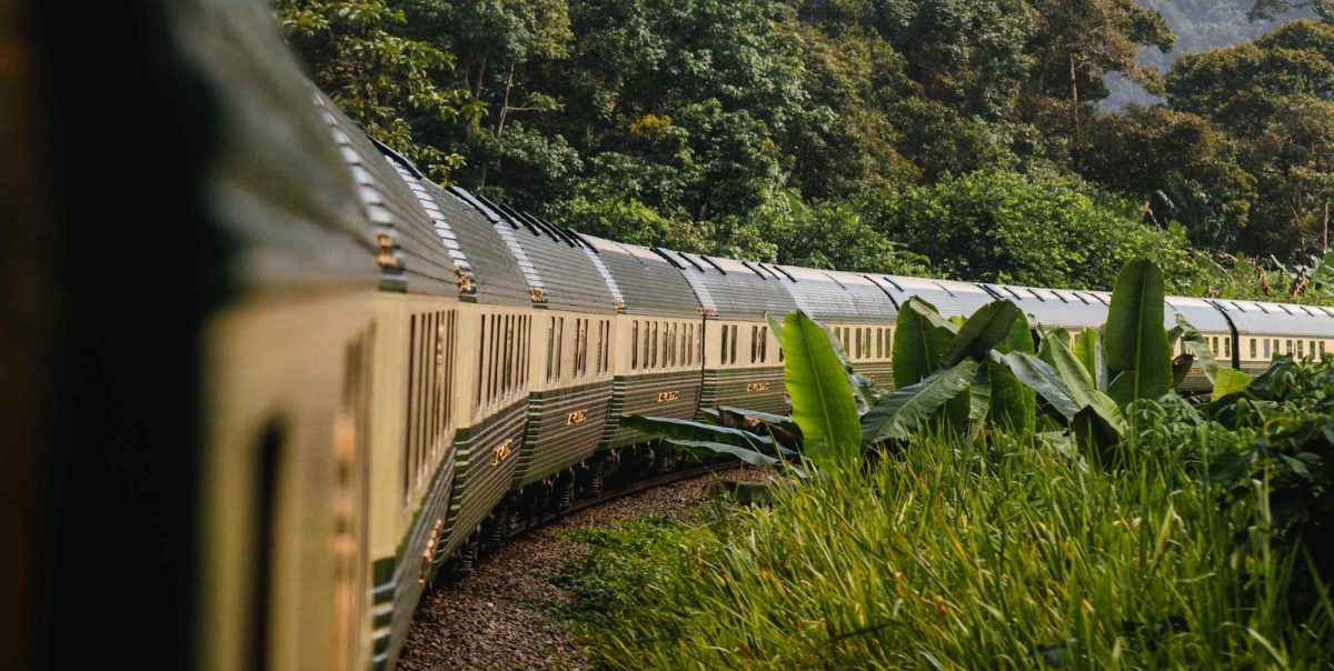 Eastern & Oriental Express green-and-cream carriages curving through Malaysian jungle