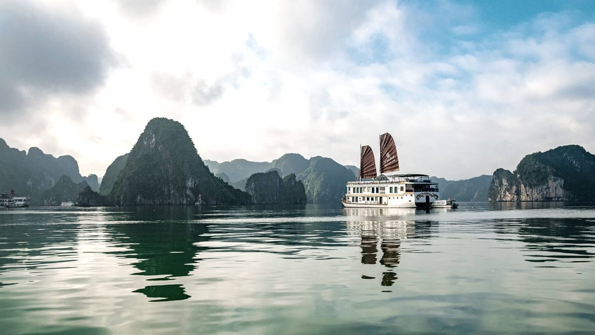 Heritage Line Violet with red sails in the calm waters of Bai Tu Long Bay