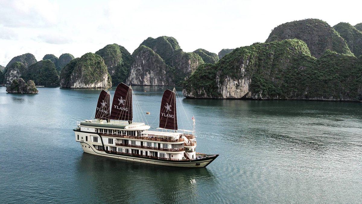 Heritage Line Ylang with three dark sails among the limestone islands of Lan Ha Bay